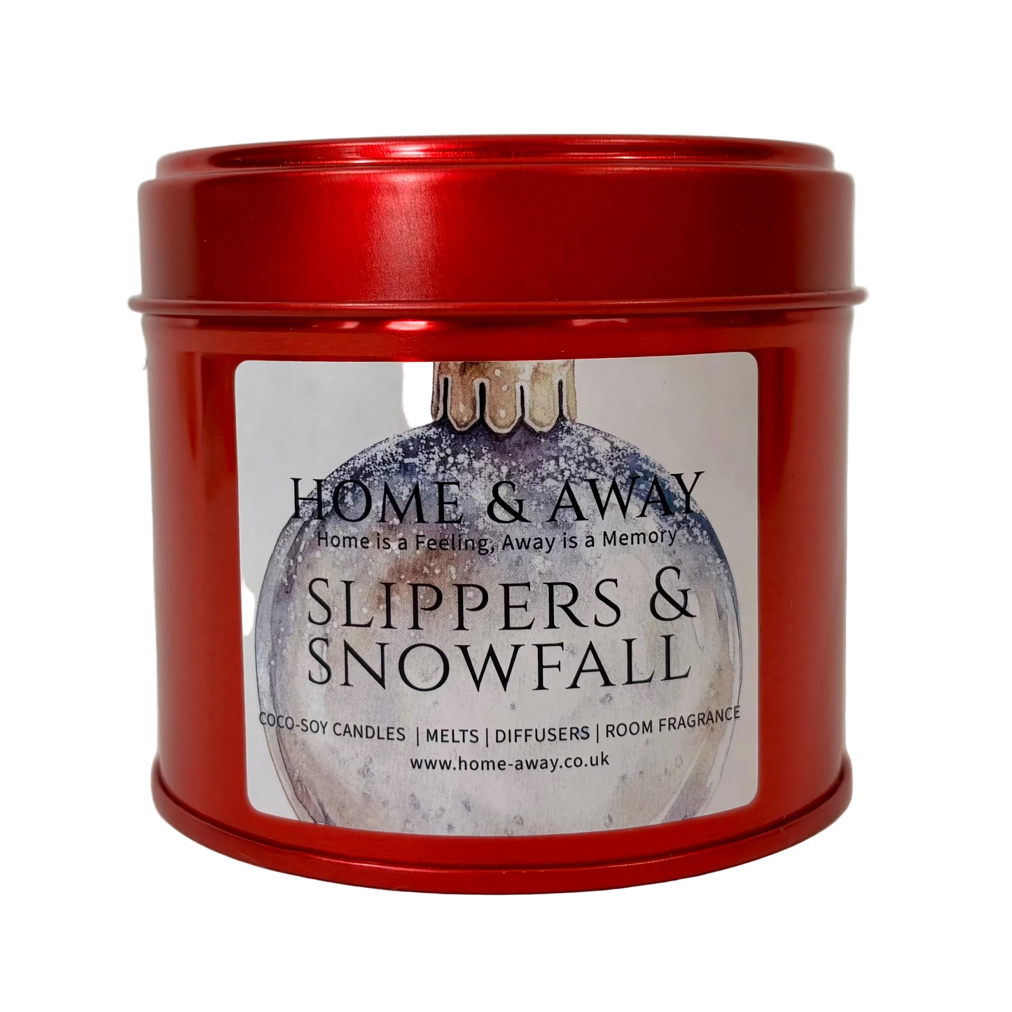 A red metal tin candle with a white label reading 'HOME & AWAY' and 'SLIPPERS & SNOWFALL' on a light neutral background.