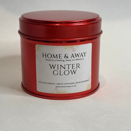 A red metal tin candle with a white label reading 'HOME & AWAY WINTER GLOW' on a light gray background.