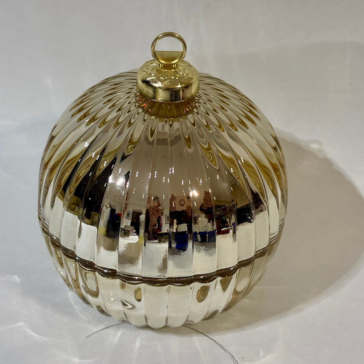 A round, ribbed glass ornament with a metallic silver finish and a gold-toned top loop, shown on a white surface with reflections.