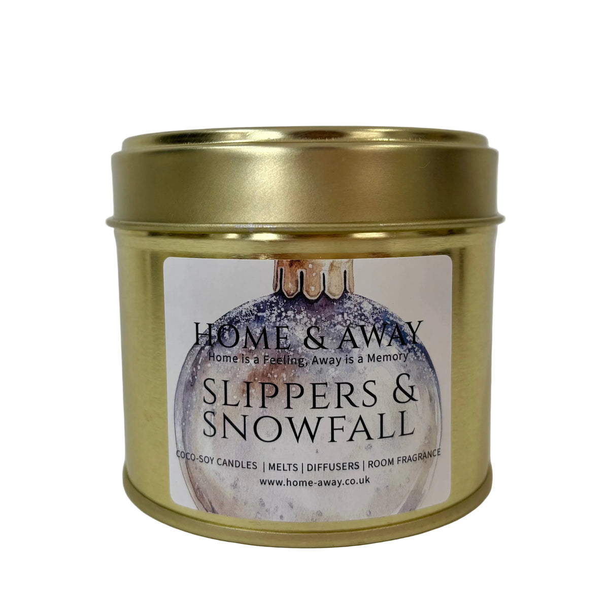 A gold metal tin candle with a white label reading 'HOME & AWAY' and 'SLIPPERS & SNOWFALL' on a plain light background.