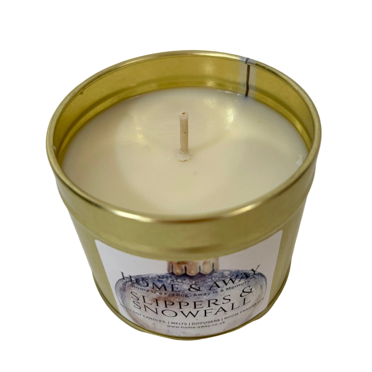 A single-wick candle in a metallic gold tin with cream-colored wax. The front label reads 'Home & Away' and 'Slippers & Snowfall'.
