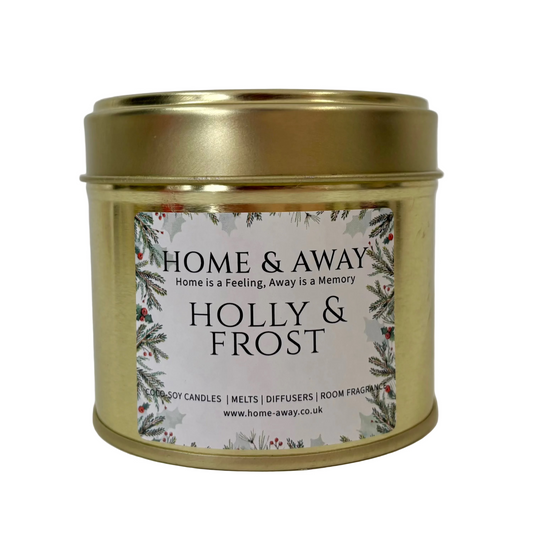 A gold metal tin candle with a white label reading 'HOME & AWAY' and 'HOLLY & FROST', photographed against a plain white background.