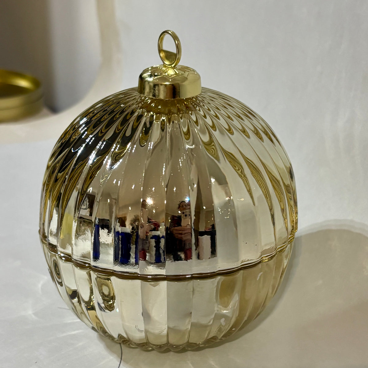 A round, ribbed glass ornament or decorative container with a gold-tone top loop and trim, photographed on a white surface against a white background.